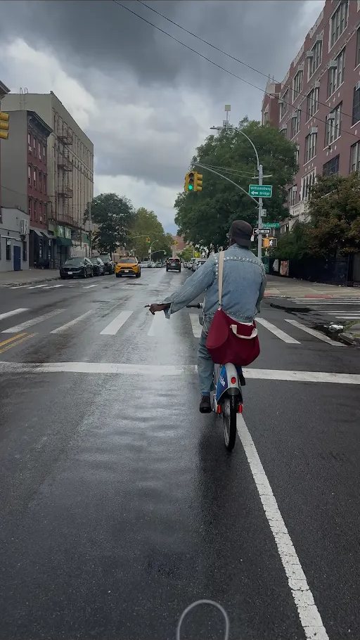Riding a Citi Bike down a wet street toward the Williamsburg Bridge
