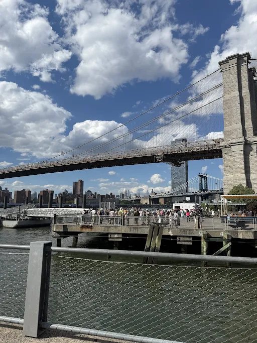 Brooklyn Bridge from the waterfront under a cloudy blue sky