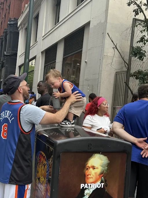 A father lifting a toddler onto a trash can to see a parade